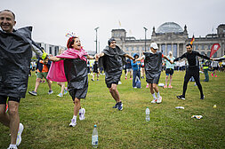 BMW BERLIN MARATHON 2023: Participants hold hands and run in a circle while warming up, the Reichstag in the background © SCC EVENTS / Sebastian Wells